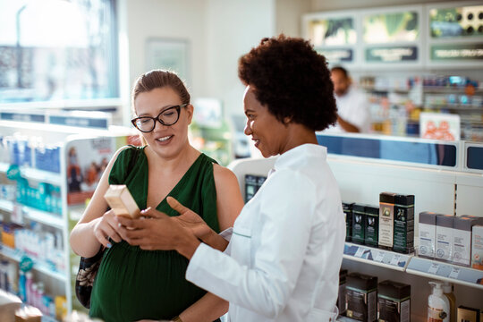 Female pharmacist helping pregnant woman in drug store