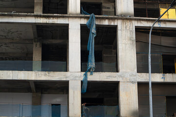 An unfinished concrete building stands tall against a cloudy sky. The exposed structure and surrounding debris depict an incomplete construction project.
