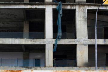 An unfinished concrete building stands tall against a cloudy sky. The exposed structure and surrounding debris depict an incomplete construction project.