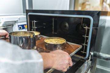 Pie making process. Raw apple tarts or pies in baking molds on a baking sheet are put by the confectioner's hands into a steam convection oven. Confectionery or production workshop.