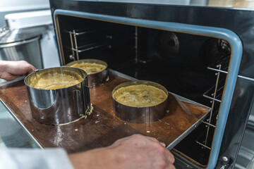 Pie making process. Raw apple tarts or pies in baking molds on a baking sheet are put by the confectioner's hands into a steam convection oven. Confectionery or production workshop.