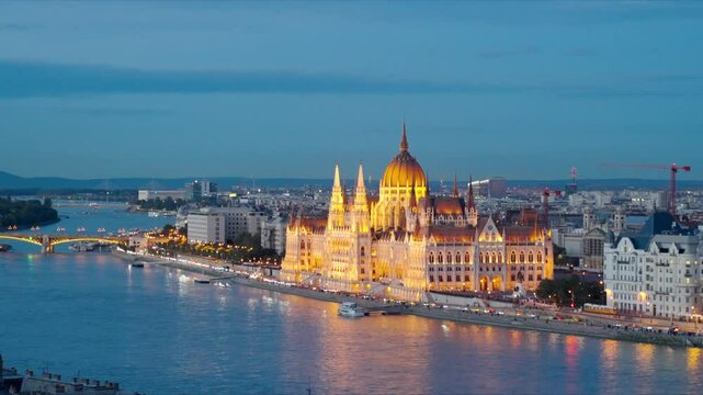 Beautiful building of Parliament in Budapest, popular travel destination with street lights glowing and boats gently drifting on the Danube River