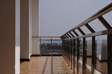 The balcony on a tall building with a silver railing is exposed to morning sunlight