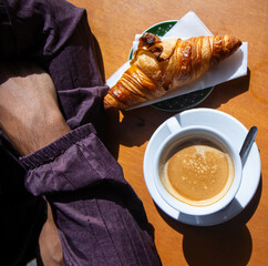 Top view of a man with his arms crossed in front of his tasty breakfast of coffee and croissant in...