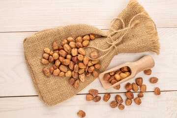 Peeled hazelnuts with jute bag on wooden table, close-up, top view.