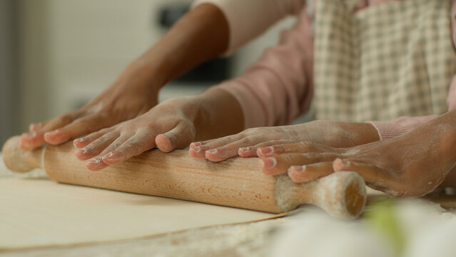 Close up cropped view hands arms African woman mother female mom teaching little child kid girl daughter cooking pastry pizza baking teach using rolling pin together at kitchen table dough cook pie