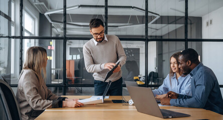 By the table. Professional workers are in the modern office together