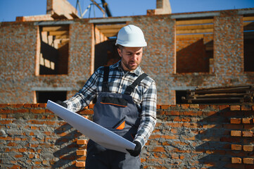 An architect or engineer on the construction of brick houses holds the construction plan in his...