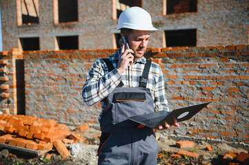 Engineer, bearded man wears safety helmet inspecting housing development project at construction...