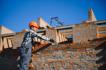 construction mason worker bricklayer installing red brick with trowel putty knife outdoors