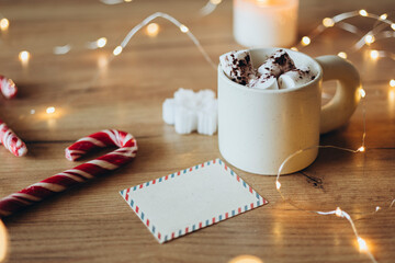 Cup of hot cocoa with marshmallows on a wooden table with Christmas lights.