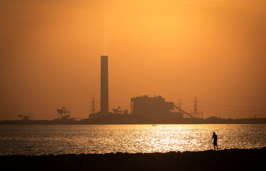Sunset, a smokestack releases emissions into the atmosphere, highlighting industrial pollution and...