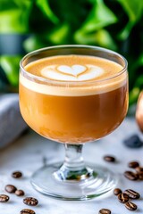  Taza baja con latte decorado con arte de espuma en forma de coraz&oacute;n. Fondo con hojas verdes y granos de caf&eacute;.
