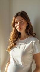 Obraz premium Woman stands by a sunlit wall, looking at the camera. Concept of natural beauty and casual style. For portrait photography.