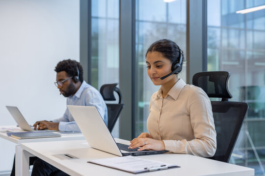 Office workers engaged in customer service tasks while using laptops. A focus on collaboration and technology is evident, showcasing a professional office atmosphere. Ideal for business imagery.