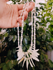 Mother of pearl necklaces in hand, holding irregular stone chokers, floral background, nacre...