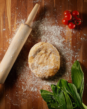 Pasta dough, salad, tomatoes and rolling pin on oak table