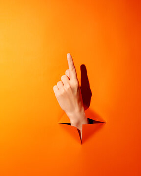 Hand points up through bright orange background