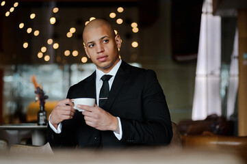 Hairless african american businessman holding cup in blurred lobby of business center