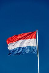 Dutch flag flies in the blue sky of amsterdam
