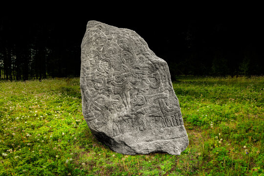 Jelling stone, replica of Harald Bluetooth's rune stone from Jelling, massive carved stone with viking inscriptions and a Jesus Christ figure on the cross, on black background, in natural environment