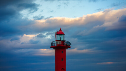 Red lighthouse, orange clouds and rough dark clouds