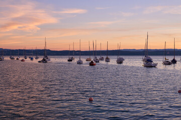 Obraz premium Sunset over Lake with Pier and Sailboats, Serene Waterfront Scene, Orange and Pink Sky, Calm Water, Silhouettes of Boats, Tranquil Evening, Reflections on Water, Peaceful Marina, Dusk Landscape