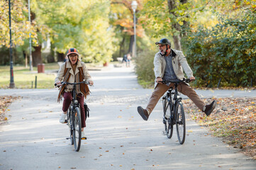 Fototapeta premium Senior couple riding bicycles together through an autumn park, laughing and enjoying an active lifestyle, showcasing fun, health, and companionship in a vibrant outdoor setting