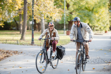 Fototapeta premium Senior couple riding bicycles together through an autumn park, laughing and enjoying an active lifestyle, showcasing fun, health, and companionship in a vibrant outdoor setting
