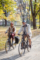 Senior couple riding bicycles together through an autumn park, laughing and enjoying an active lifestyle, showcasing fun, health, and companionship in a vibrant outdoor setting