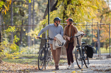 Obraz premium Smiling senior couple with their bicycles in a sunny autumn park, enjoying an active and healthy lifestyle surrounded by nature and warmth