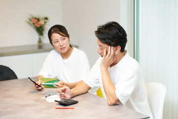 銀行口座の通帳とスマートフォンを見て考え込む男女