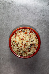 Earthenware bowl full of long, red, wild rice on a kitchen countertop in a zenithal photograph