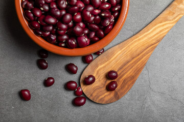 Earthenware bowl full of Anguiano red beans with a wooden spoon on a kitchen worktop in a zenithal photograph.