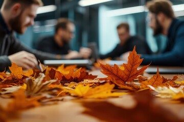 A close-up of autumn leaves on a table with blurred figures engaged in discussion, creating a warm, collaborative atmosphere.