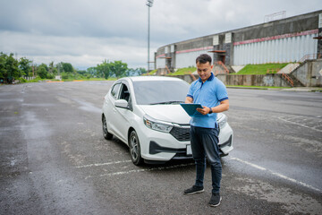 A man is inspecting a vehicle in an empty parking lot, focusing on its maintenance