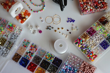 Hand figurine, colorful friendship bracelets, necklaces, various beads and DIY supplies on the table. Making jewelry at home. Selective focus.