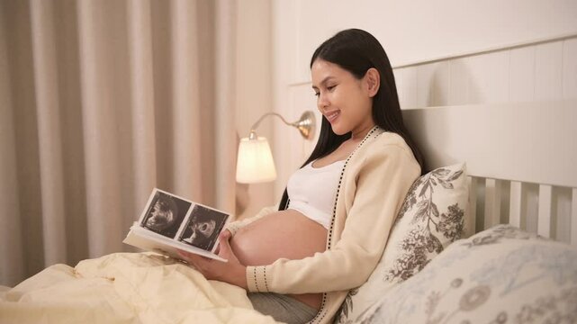 Pregnant woman holding ultrasound picture in bedroom