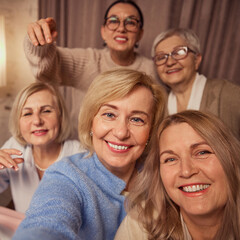 Obraz premium Selfie portrait of five cheerful, smiling elderly women, friends, taking selfie, meeting at home for cozy celebrations and wine drinking. Concept of elderly lifestyle, positive emotions