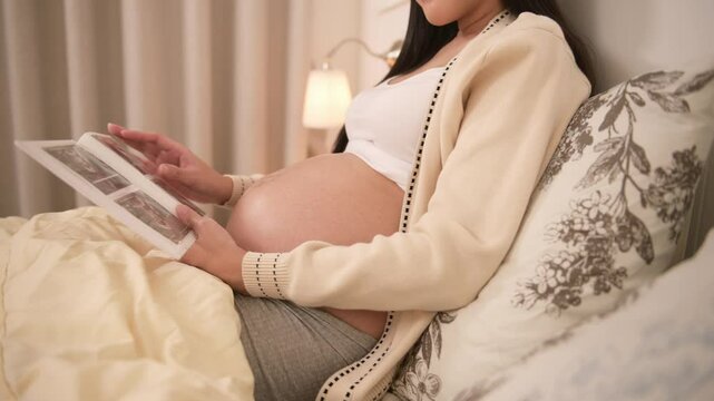 Pregnant woman holding ultrasound picture in bedroom