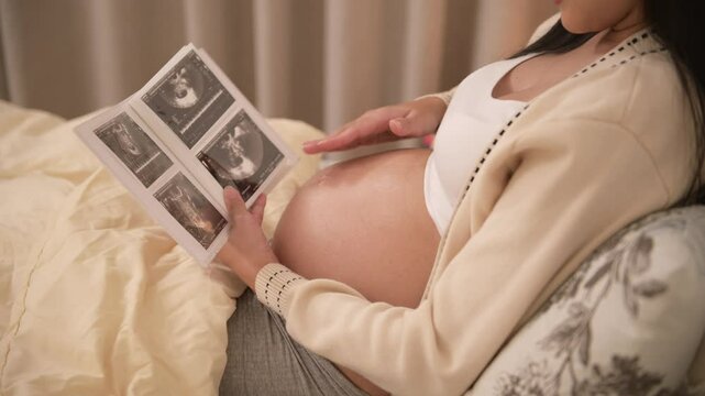 Pregnant woman holding ultrasound picture in bedroom