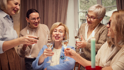 Emotional elderly women, friends meeting at home, in cozy living room, cheerfully talking, discussing news, drinking wine. Concept of elderly lifestyle, positive emotions