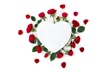 Red flowers roses, petals and paper card note in the shape heart on white background. Top view, flat lay