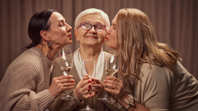 Happy Mothers day. Two elderly women, daughter's greeting their old mother with her day, drinking wine, laughing, showing respect and love. Concept of elderly lifestyle, positive emotions - Powered by Adobe
