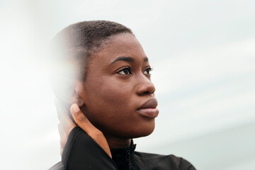 young contemplative ethnic female with short hair touching face in daylight, flare effect