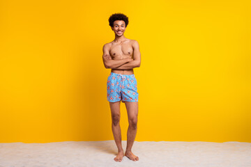 Young man smiling confidently in stylish swimwear against vibrant yellow background, embodies...