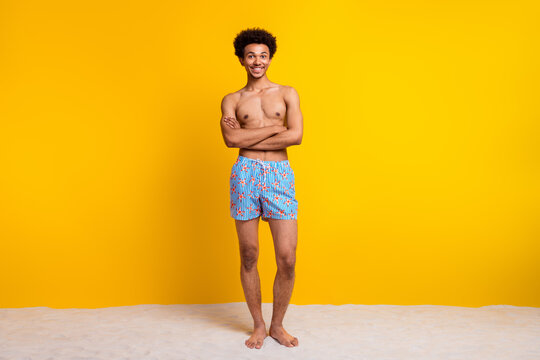 Young man smiling confidently in stylish swimwear against vibrant yellow background, embodies summer fashion and casual lifestyle