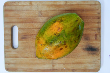 A papaya papaw or pawpaw  fruit lying on a wooden cutting board
