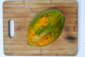 A papaya papaw or pawpaw  fruit lying on a wooden cutting board