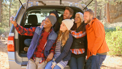 Group Of Friends Outdoors Posing For Selfie Sitting In Open Tailgate Of Car Before Autumn Walk 